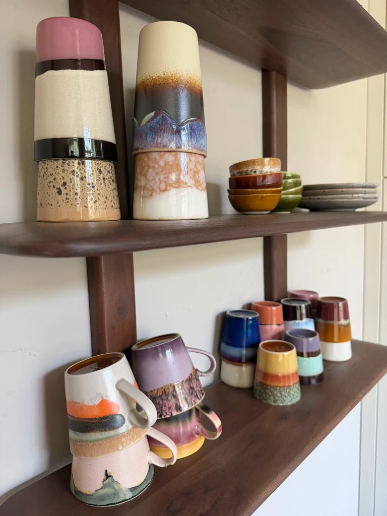 Verzameling kleurrijke HKLIVING-koffiekopjes op een donkerhouten wandrek