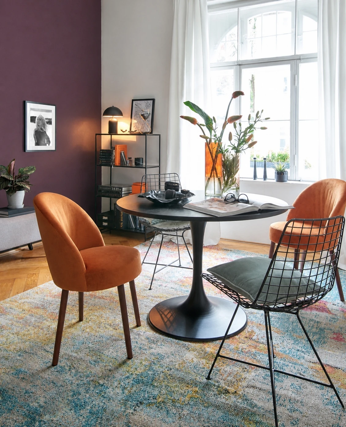 Eethoek met een patroonvloerkleed, oranje stoelen en een warme pruimkleurige wand